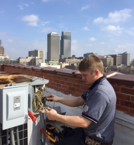 Fred's commercial AC repair technician fixing rooftop unit in city