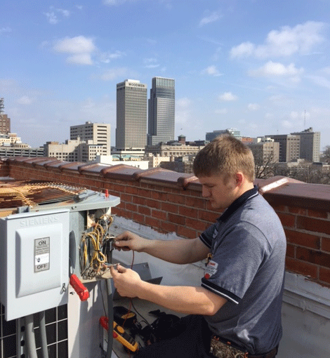 Fred's commercial AC repair technician fixing rooftop unit in city